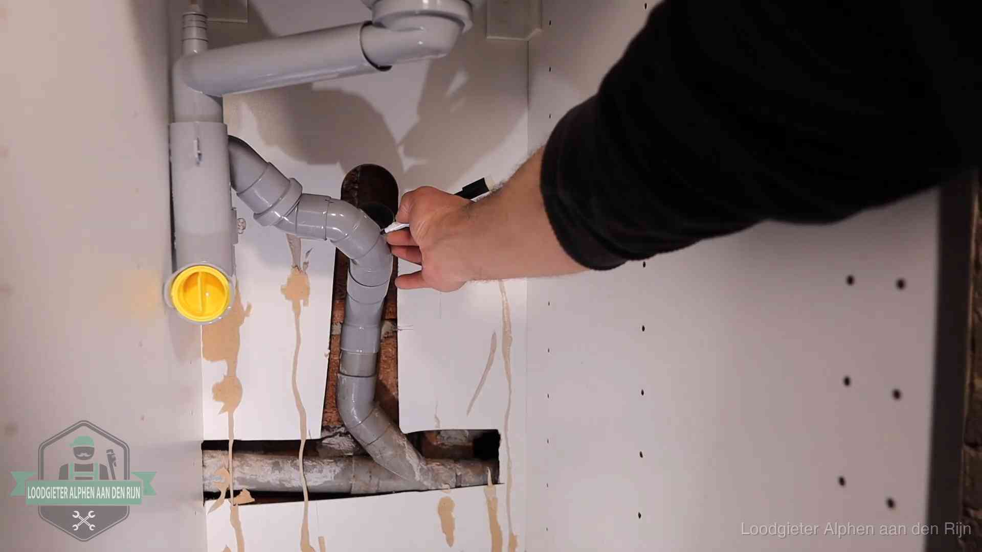 Loodgieter markeert een pvc-afvoerbuis onder een gootsteen in Alphen aan den Rijn