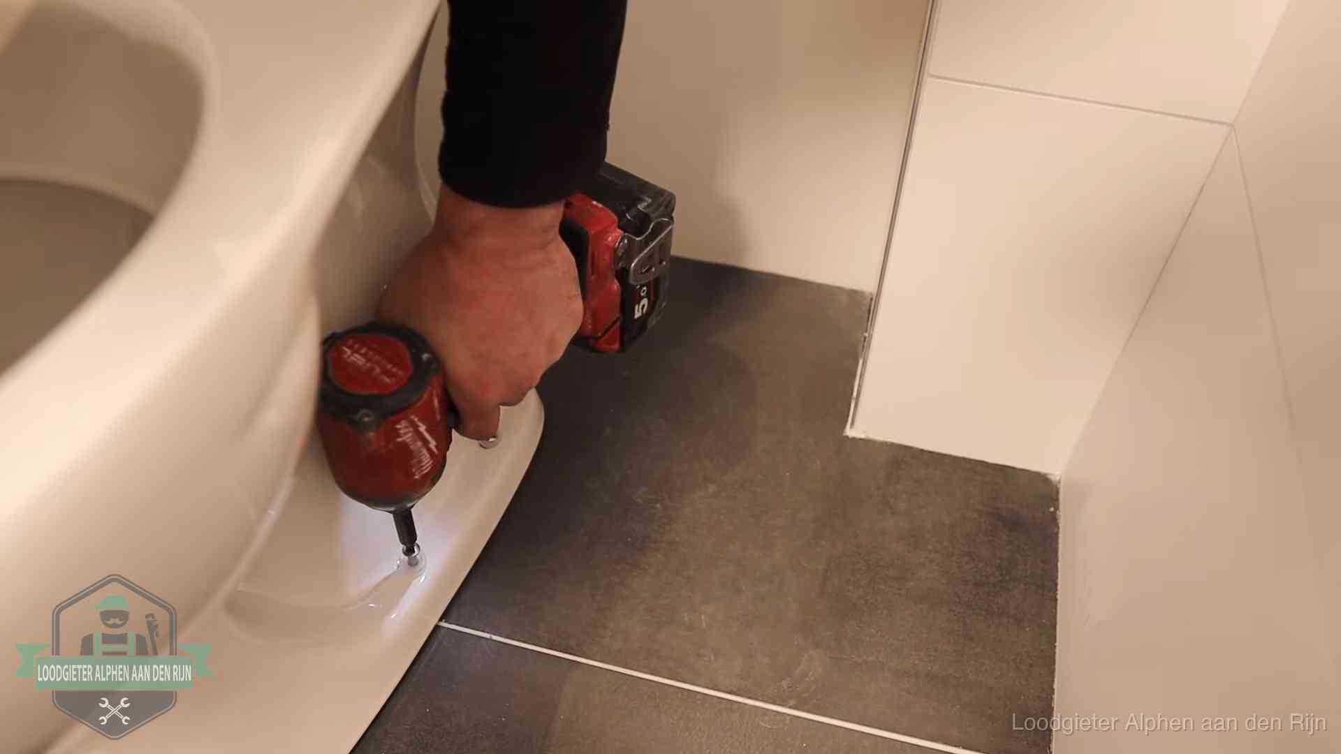 Loodgieter zet de voet van een wc-pot vast op de tegelvloer in Alphen aan den Rijn